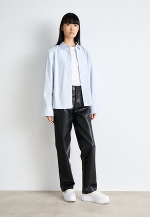Camicia a maniche lunghe azzurro chiaro, maglietta bianca a girocollo, pantaloni in pelle nera e sneakers bianche. Design semplice, texture liscia e vestibilità rilassata.