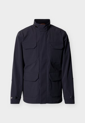 Temno mornarsko modra jakna z visokim ovratnikom, štirimi sprednjimi žepki z zaponkami in zapenjanimi manšetami, prikazana na enostavni svetli podlagi.