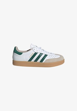 White sneakers with green stripes, suede accents, and a gum rubber sole. Features perforated toe and flat white laces. Brand name displayed.
