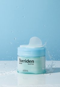 En gennemsigtig grøn krukke med et lyseblåt låg, mærket "Torriden Dive In Multi Pad," har en pude, der stikker op, mens vand sprøjter omkring.