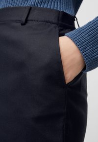 Jupe en tissu noir avec une texture lisse, dotée d'une poche latérale et d'une taille. Le haut est un pull en tricot côtelé bleu.