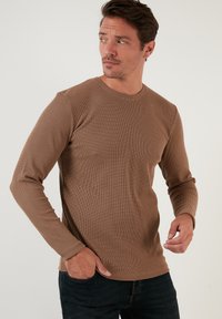 Braun gestreifte Langarmshirt in einer figurbetonten Passform, mit Rundhalsausschnitt und strukturiertem Stoff, kombiniert mit dunklen Jeans.