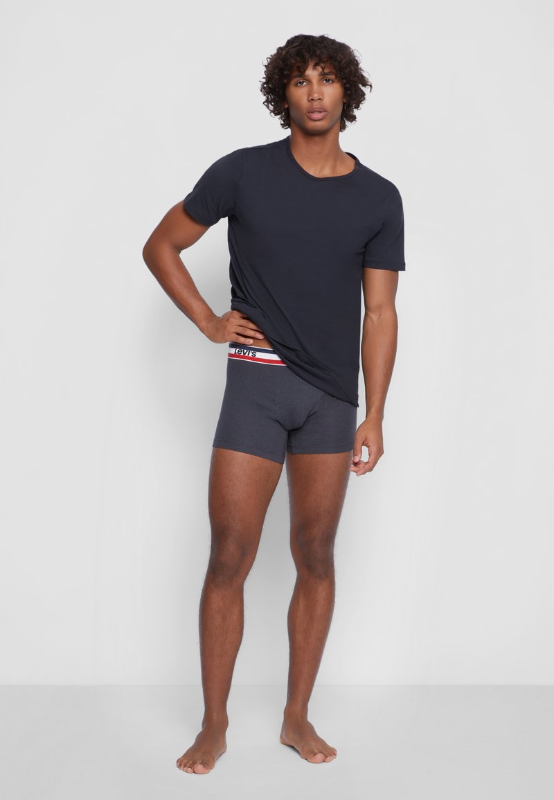 Marineblaues Kurzarm-T-Shirt mit Rundhalsausschnitt, kombiniert mit dunkelgrauen Boxer-Shorts, die ein rotes und weißes Logoband haben.