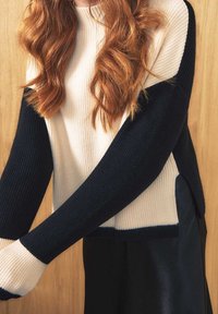 Pull en tricot côtelé avec un corps crème et des manches bleu marine, présentant une coupe décontractée et des poignets blancs contrastants. Design minimaliste.