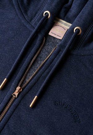 Navy blue zip-up hoodie with metal zipper and drawstrings, embroidered "Superdry" logo, and inside label reading "Premium Grade Vintage Sweat."