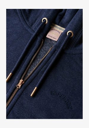 Navy blue zip-up hoodie with metal zipper and drawstrings, embroidered "Superdry" logo, and inside label reading "Premium Grade Vintage Sweat."