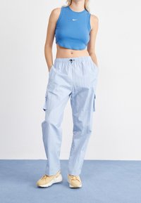 Svetle modré cargo kalhoty s elastickým pasem a bočními kapsami, kombinované s modrým tílkem bez rukávů s bílým logem. Neutrální tenisky.