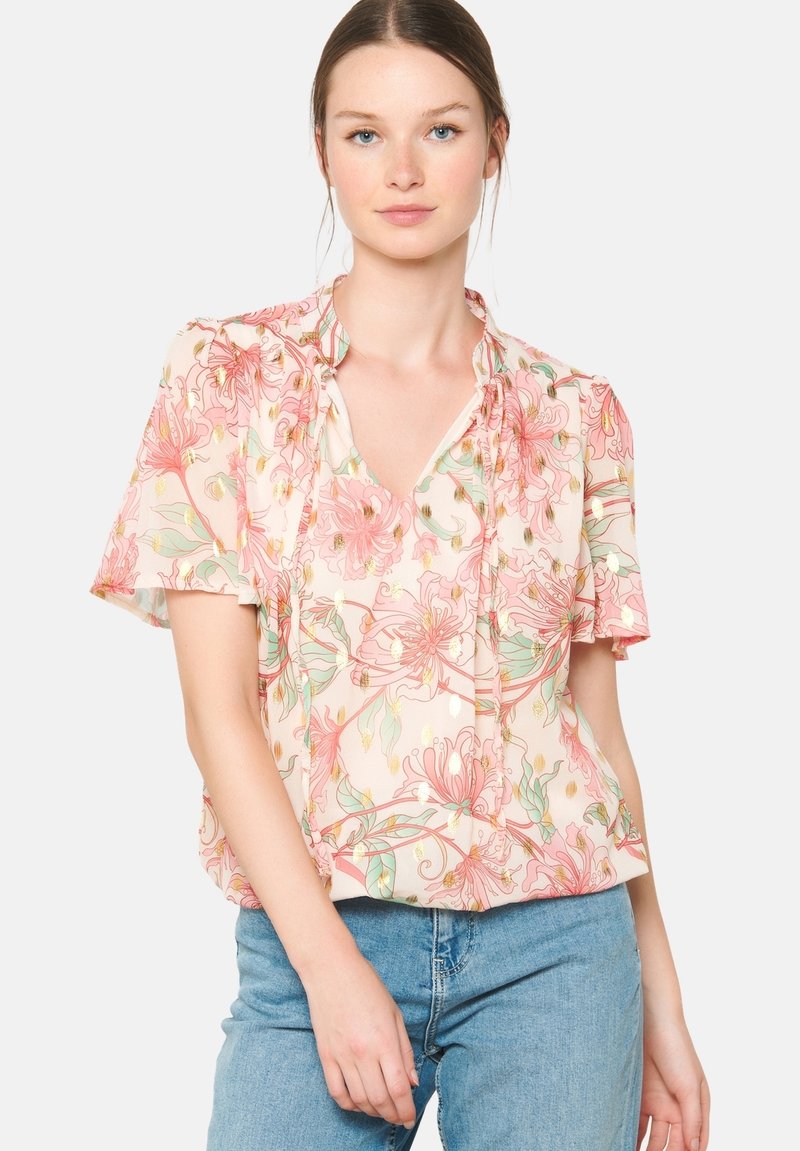 Kwiatowa bluzka w jasnoróżowym kolorze z krótkimi, falbaniastymi rękawami, dekoltem w serek i złotymi akcentami. Posiada luźny krój oraz delikatny wzór kwiatowy.