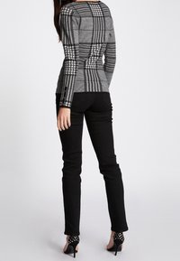 Pantalones ajustados negros combinados con una blusa gris de cuadros ceñida que presenta patrones y texturas variadas, mostrados desde una vista trasera.