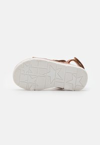 Brown suede sandal with a white rubber sole featuring a star pattern, adjustable strap, and textured tread for grip.