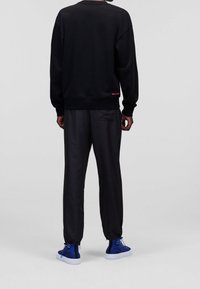 Felpa nera con collo a giro, maniche lunghe e orlo a costine, abbinata a pantaloni neri con polsini elasticizzati e sneakers blu.
