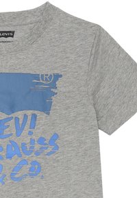 T-shirt in cotone grigio con un design grafico blu che presenta testo e un simbolo di marchio registrato. Maniche corte e scollatura rotonda.