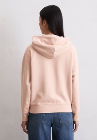 Felpa rosa chiaro con cappuccio e texture morbida, caratterizzata da una vestibilità comoda. Abbinata a jeans in denim blu, che mostrano elementi di design semplici.