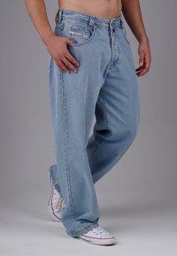 Hellblaue Denim-Jeans mit lockerer Passform, traditionellem Five-Pocket-Design und Kupferbeschlägen. Getragen mit weißen Turnschuhen.