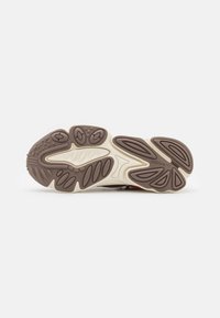 Adidas sneaker sole features a textured brown rubber surface with a light cream border, curved patterns, and logo detail integrated into the design.