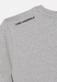 Pelēks džemperis ar apaļu kakla izgriezumu, maigu tekstūru un melnu "KARL LAGERFELD" logo, kas ir izšūts aizmugurē.