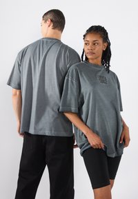 Graue Baumwoll-T-Shirts mit kurzen Ärmeln und lockerem Schnitt. Ein Shirt hat einen grafischen Druck auf der Brust. Getragen mit schwarzen Shorts.