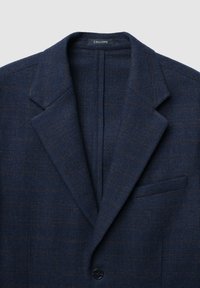 Blazer blu navy realizzato in tessuto testurizzato con un sottile motivo a scacchi, chiusura a singolo bottone e tasca sul petto. Etichetta del marchio visibile all'interno.