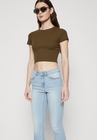 Olíva zöld, rövidített póló és világoskék, skinny farmernadrág. A pólón bordázott textúra található, míg a farmernadrág klasszikus öt zsebes kialakítással rendelkezik.