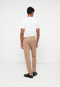 Beige bukser med en skræddersyet pasform, som har baglommer og er parret med en simpel hvid t-shirt, der fremhæver et minimalistisk design.