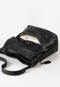 Schwarze Leder-Umhängetasche mit offenen Klappen, die ein hell gemustertes Innenfutter und Magnetknopfverschlüsse zeigt.