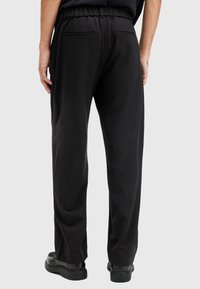 Pantalones negros con cintura elástica y bolsillos traseros, presentan un corte relajado y una textura suave, adecuados para un uso casual o relajado.