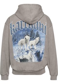 Sudadera con una escena de bosque invernal que presenta dos lobos blancos de pie sobre rocas nevadas, con un gran texto estilizado encima de ellos.