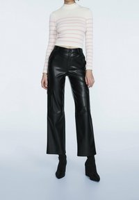 Vit ribbad croptopp med rosa ränder, tillsammans med högmidjade svarta byxor i konstläder med vida ben och svarta klackstövlar med blockklack.