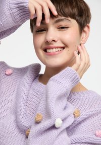 Hellblauer Strickpullover mit weitem Ausschnitt und strukturiertem Muster, versehen mit dekorativen Pompoms in Rosa, Beige und Weiß an den Ärmeln.