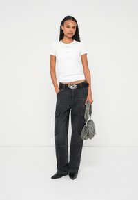 T-shirt branca justa, calças cargo cinzentas com bolsos, cinto preto com fivela prateada e uma mala texturizada cinzenta. Sapatos pretos pontiagudos.