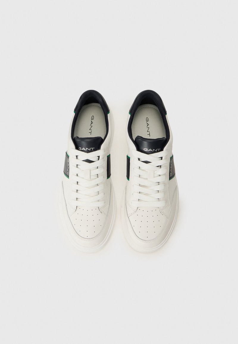 Weiße Leder-Sneaker mit perforierter Zehenpartie, schwarzen Akzenten und grünen Details. Eine dicke Sohle und runde Schnürsenkel runden das Design ab.
