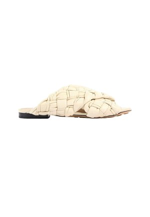 Sandalia plana beige con una gran tira de cuero trenzado y un pequeño tacón negro.
