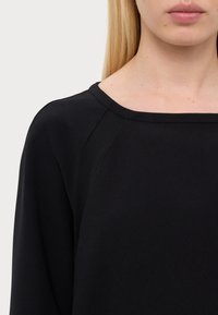 Crna majica s okruglim izrezom i raglan rukavima. Glatka tekstura, minimalistički dizajn i bez vidljivih uzoraka ili ukrasa.