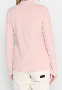 Hellrosa Fleecepullover mit langen Ärmeln und Stehkragen, ausgestattet mit einem dezenten Logo am Halsausschnitt und abgerundetem Saum für Komfort.