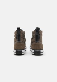 Sneaker alte in suede marrone con accenti neri, suola in gomma bianca e dettagli in logo embossato sul tallone. Presentano un collo imbottito e un linguetta per il tiraggio.