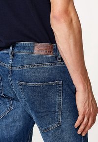Mörkblå denimjeans med en texturerad yta, utrustade med en brun läderetikett vid midjan och två bakfickor.