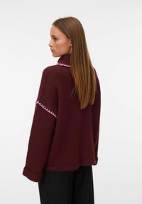 Pull en tricot bordeaux avec un col haut, ornée de coutures roses le long des épaules et des manches, et avec une coupe décontractée.