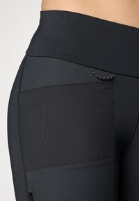 Zwarte leggings met een hoge tailleband, voorzien van een gestructureerde zijzak en gladde stof, ontworpen voor comfort en flexibiliteit.