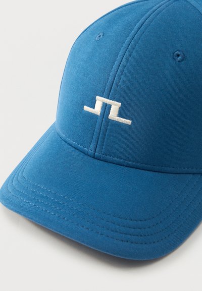 Μπλε καπέλο μπέιζμπολ με λευκό κεντημένο αφηρημένο λογότυπο στο μπροστινό πάνελ, με ραμμένες λεπτομέρειες και οπές αερισμού.