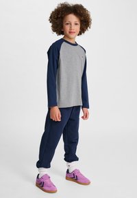 Graues und marineblaues Langarmhemd, marineblaue Hose und lila Turnschuhe. Bietet weichen Stoff, eine lockere Passform und ein kleines Logo-Detail auf dem Hemd.