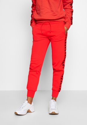 Röda sweatpants i mjukt tyg, med svarta sidostreck och logodetaljer, elastisk midja och feste anklar. Matchas med vita sneakers.