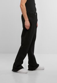 Pantaloni din denim negri, cu un design drept, tiv destrămat și stil cu cinci buzunare, asortați cu teniși albi.