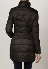 Vadderad kappa i mörkbrunt med hög krage. Har horisontell sömnad, medellång design och en slät, glänsande yta.