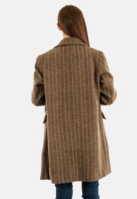 Abrigo marrón con estampado de espiga, de mangas largas, con solapa de muesca y bolsillos laterales, combinado con jeans de mezclilla azul oscuro.