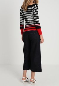 Zwart-wit gestreepte gebreide sweater met rode accenten, gecombineerd met donkere wijde jeans en witte hoge hakken.