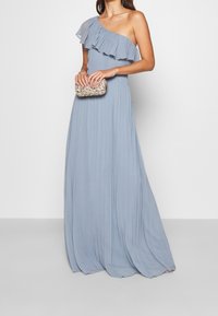 Robe bleu clair à une épaule avec des volants et une texture plissée. Associée à une petite pochette argentée étincelante. Design simple et élégant.