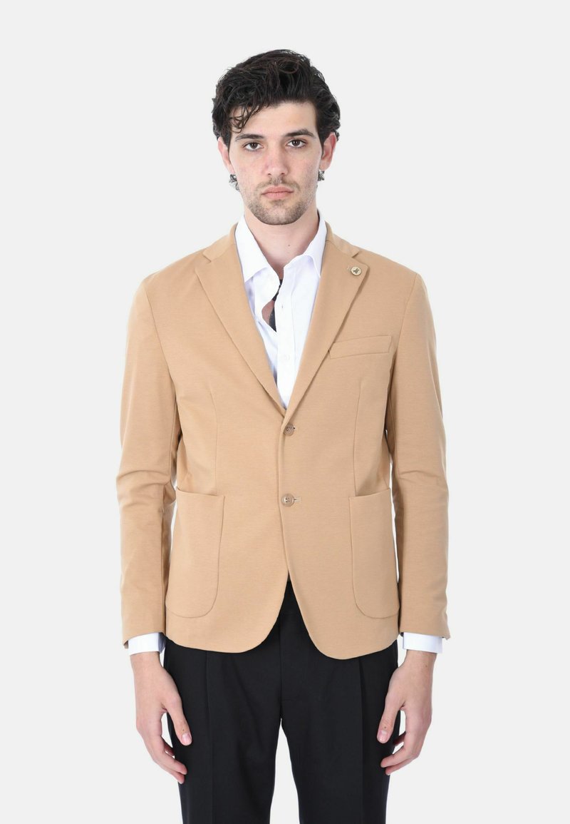 Blazer beige in tessuto leggero, con chiusura a singolo bottone, tasche frontali e rever a scollo, abbinato a una camicia bianca.