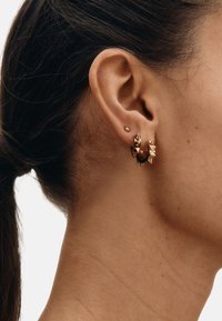 Gold hoop earrings with spikes, featuring a shiny texture and small stud earring. Worn on the right ear.