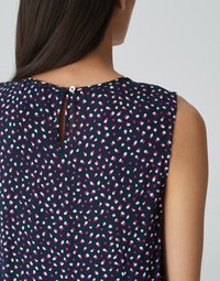 Marineblauw top met een stippenpatroon in roze en wit. Voorzien van een open rug met een knoopsluiting en een mouwloos ontwerp.