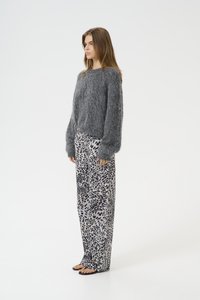 Maglione grigio fluffy con maniche lunghe abbinato a pantaloni larghi con una stampa animale nera e grigia. Sandali semplici completano il look.